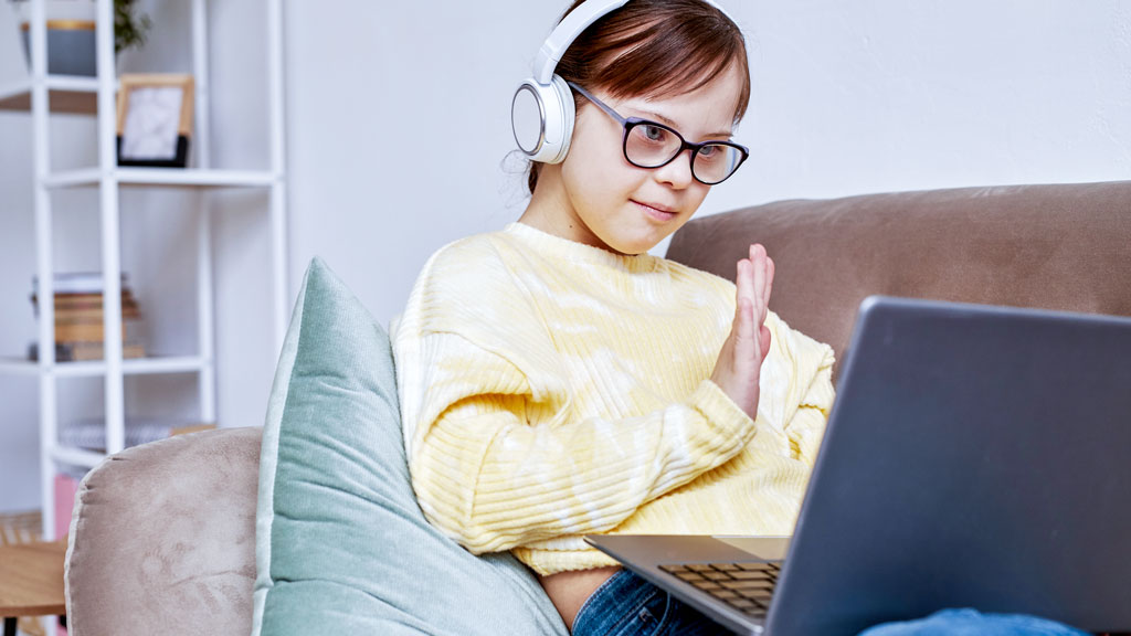 Porträt eines Mädchens mit Trisomie 21, das in einer Online-Unterrichtsstunde in die Kamera winkt.