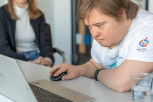 Porträt eines Mädchens mit Trisomie 21, das in einer Online-Unterrichtsstunde in die Kamera winkt.