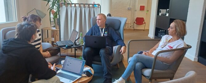 Mehrere Teilnehmende sitzen mit Laptops in einer hellen Sitzecke und diskutieren gemeinsam während des Hackathons.